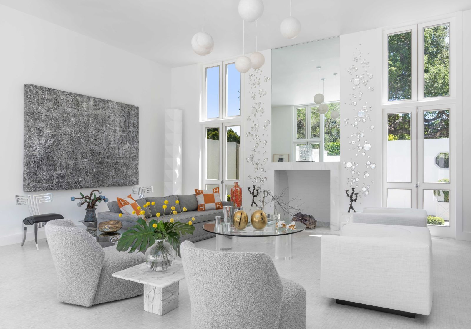 The white living room of a significant modernist home, with high-end furnishings and floor to ceiling windows and glass doors.